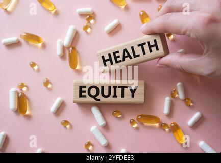 Health Equity symbol. Wooden blocks with words Health Equity. Beautiful pink background with pills. Doctor hand. Medicine and Health Equity concept. C Stock Photo