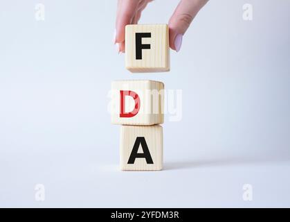 FDA - Food Drug Administration symbol. Wooden cubes with word FDA. Doctor hand. Beautiful white background. Medical and Food Drug Administration conce Stock Photo