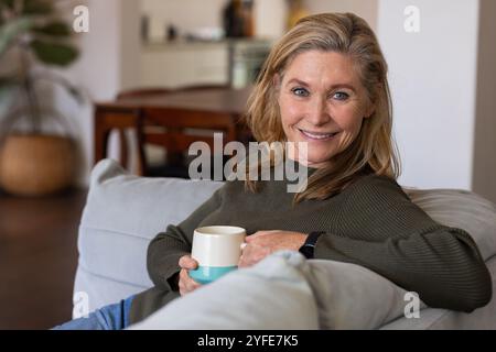 Smiling senior woman relaxing on sofa at home with coffee mug Stock Photo