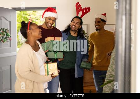 multiracial friends celebrating Christmas at home, exchanging gifts and wearing festive hats Stock Photo