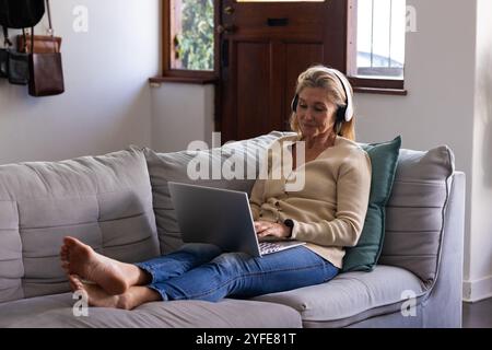 Relaxing on sofa, senior woman using laptop and headphones at home Stock Photo