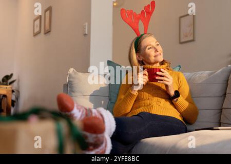 Christmas time, Relaxing at home, senior woman wearing reindeer antlers enjoying hot drink Stock Photo
