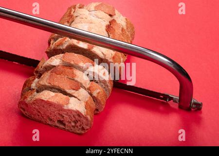 Creative Concept of Sliced Bread with Hacksaw on Red Background - Unique Image for Art, Abstract, and Food-Related Visuals Stock Photo