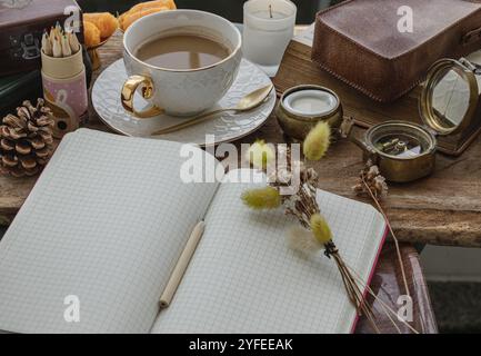 Refreshing with Hot coffee in ceramic cup  served with Fresh milk on old wooden worktable with notebook, pencil, colored pencils, dried flowe, small h Stock Photo