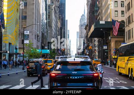 A busy street scene in New York City features pedestrians crossing, vehicles including yellow taxis and a school bus, and skyscrapers. Stock Photo