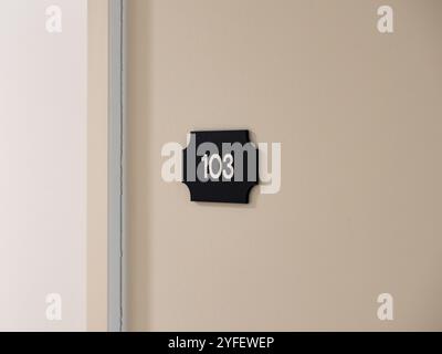 Number 103 on a house wall. The one hundred and three is a room number in a hotel building. The figures are in white on a black background. Stock Photo