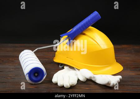 Yellow hard hat, paint roller and rubber gloves on wooden table Stock Photo