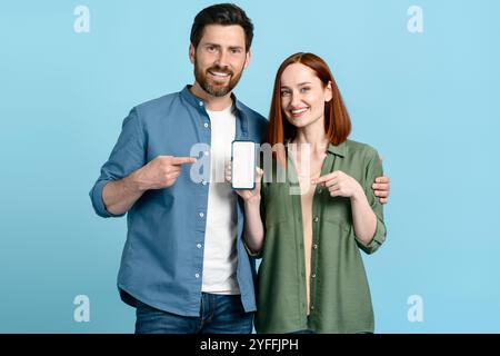 Smiling couple pointing at smartphone with empty screen for your advertisement or promotional text Stock Photo