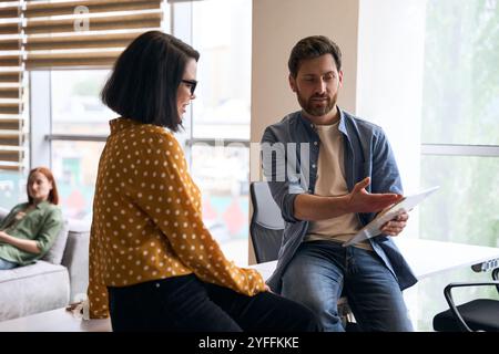 Businessman explaining new project to colleague, showing presentation on digital tablet, working together in modern office Stock Photo