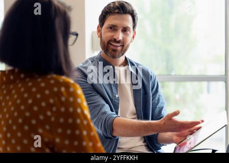 Businessman is sharing ideas with a colleague during a meeting, gesturing with his hand as he shows her something on a tablet Stock Photo