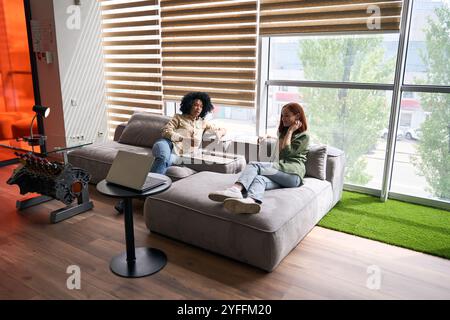 Two businesswomen having a casual business meeting while relaxing on a comfortable sofa during a break in their modern office Stock Photo