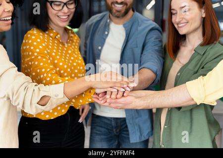 Team of happy young business people is joining hands in the office, showing their unity and teamwork Stock Photo