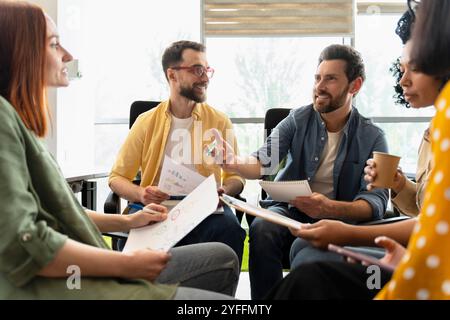 Diverse team of professionals is having a productive meeting, engaging in a lively discussion about financial charts and documents Stock Photo