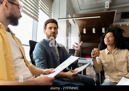 Team of business colleagues is having a meeting in the office, holding charts and discussing statistics Stock Photo