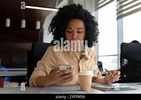 Businesswoman is working in the office, checking her smartphone and taking notes on a document Stock Photo