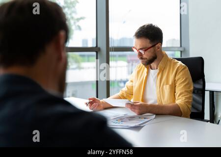 Businessman is reviewing financial data on his tablet during a meeting with a colleague, demonstrating focused concentration Stock Photo