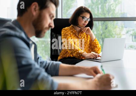 Businesswoman concentrating while using laptop at desk and businessman working in foreground Stock Photo