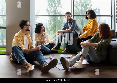 Diverse team of professionals is having a productive brainstorming session, sitting on the floor and discussing new ideas Stock Photo