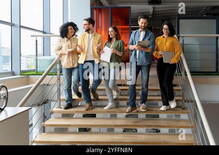Diverse group of business people are having a discussion while walking down a staircase in a modern office Stock Photo