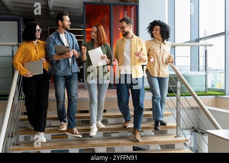 Five young professionals are walking down stairs in a modern office while having an informal meeting Stock Photo