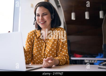 Cheerful businesswoman wearing headset is having a video call on laptop in the office Stock Photo