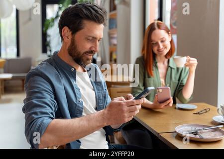 Couple using smartphones while having coffee in a cafe, enjoying a moment of relaxation and connection Stock Photo