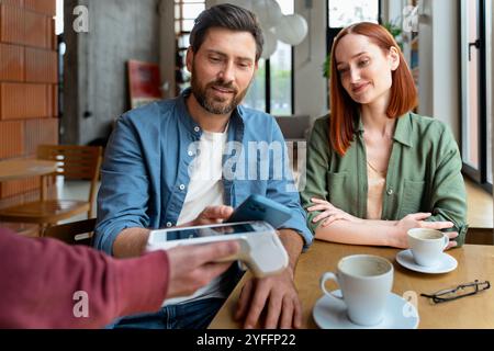 Couple is paying their bill in a cafe using a smartphone for a contactless payment Stock Photo