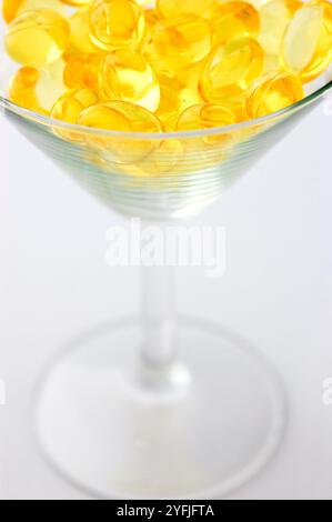 Golden cod liver fish oil soft gel capsules, pills in martini glass, translucent yellow health supplements in creative healthcare still life concept Stock Photo