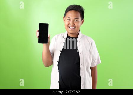 Young Indonesian Boy Holding Black Screen of Mobile Cell Phone, Isolated on Yellow Background Stock Photo