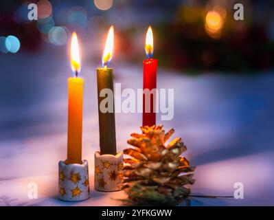 Three burning advent candles in decorative holders with pine cones and festive bokeh background. Stock Photo