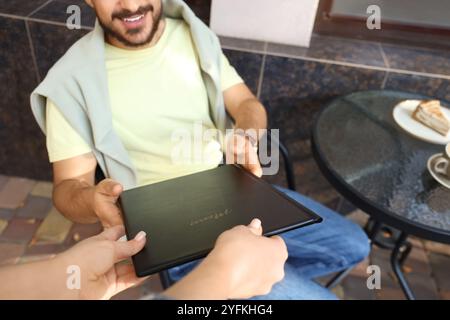 Young man taking menu from waitress in street cafe Stock Photo