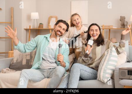 Happy family with microphones and ukulele singing karaoke on sofa at home Stock Photo