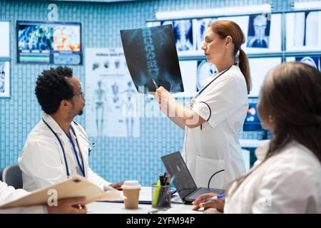 Doctor showing the x ray scan results to her colleagues in a meeting, people with expertise collaborating on treatment options based on diagnostic. Disease prevention strategies with radiography. Stock Photo