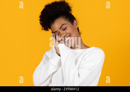 Smiling young woman posing joyfully against a bright yellow background Stock Photo