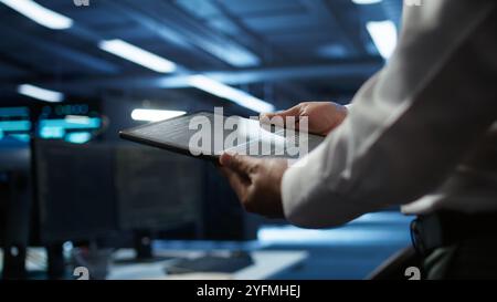 Data center admin responsible for installation of networking systems solving tasks in workspace. Close up of tablet used by IT worker doing maintenance on server farm gear, camera B Stock Photo