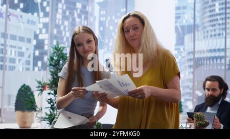 Clients looking over statistical charts given by financial advisor analyzing market trends and providing informed recommendations to optimize their income. Women reading investment plan, camera B Stock Photo