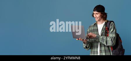 Online education. Teenage student with backpack using laptop for e-learning, turquoise background Stock Photo