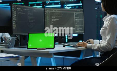 Data center developer responsible for installation of networking equipment solving tasks on green screen device. Woman doing maintenance on server room infrastructure using chroma key tablet, camera A Stock Photo