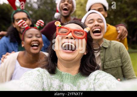 Christmas time, taking a selfie, laughing together outdoors, multiracial friends in park Stock Photo