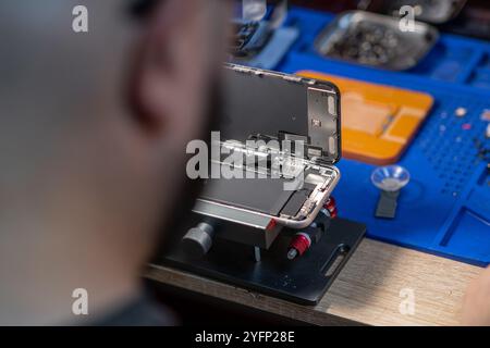 A technician meticulously replaces a smartphone battery in a well-equipped workshop with various tools nearby Stock Photo