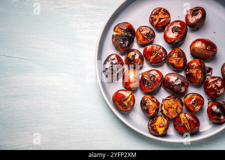 Roasted chestnuts on a blue plate on a light blue wooden background. Space for text. High quality photo Stock Photo