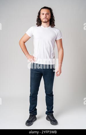 A young man with curly hair stands confidently against a neutral background Stock Photo