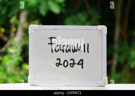 handwritten text "Farewell 2024" on white chalkboard with blurred forest background Stock Photo
