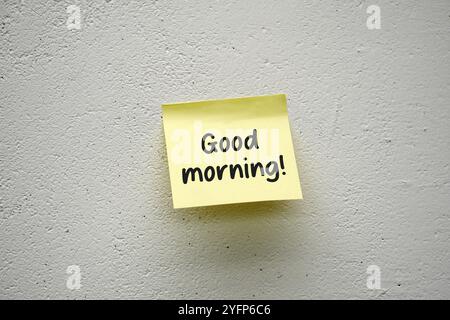 Yellow stick note with handwritten text Good morning on a white cement wall Stock Photo