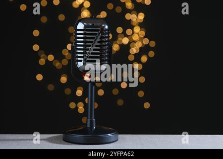 Vintage microphone on table against black background with blurred lights. Sound recording and reinforcement Stock Photo