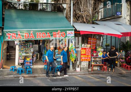 Two men walk out of a small shop selling iced tea and groceries on Yen Phu Street in Hanoi, Vietnam Stock Photo