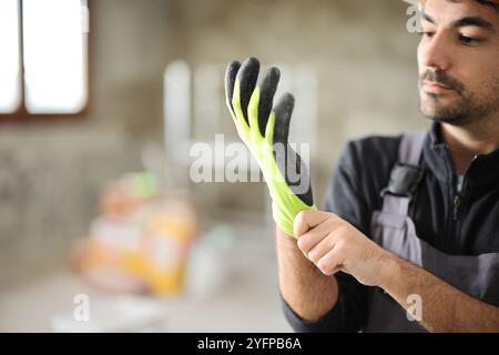 Construction worker putting on protective gloves in a house under renovation Stock Photo