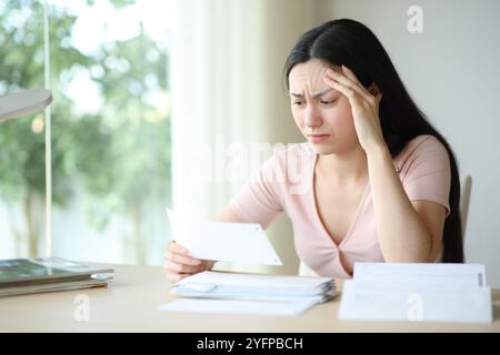 Worried asian woman complaining checking paper invoice sitting at home Stock Photo
