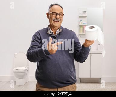 Smiling mature man pointing at roll of toilet paper in a bathroom Stock Photo