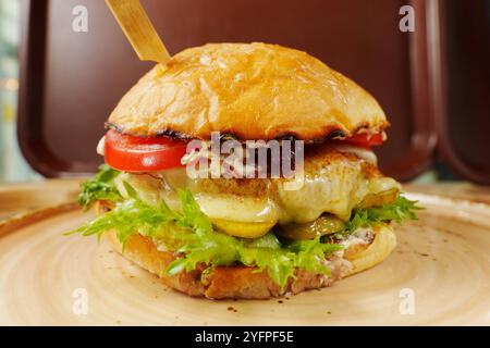 A mouthwatering cheeseburger stacked high with fresh toppings, nestled on a rustic plate ready to be enjoyed in a cozy setting Stock Photo